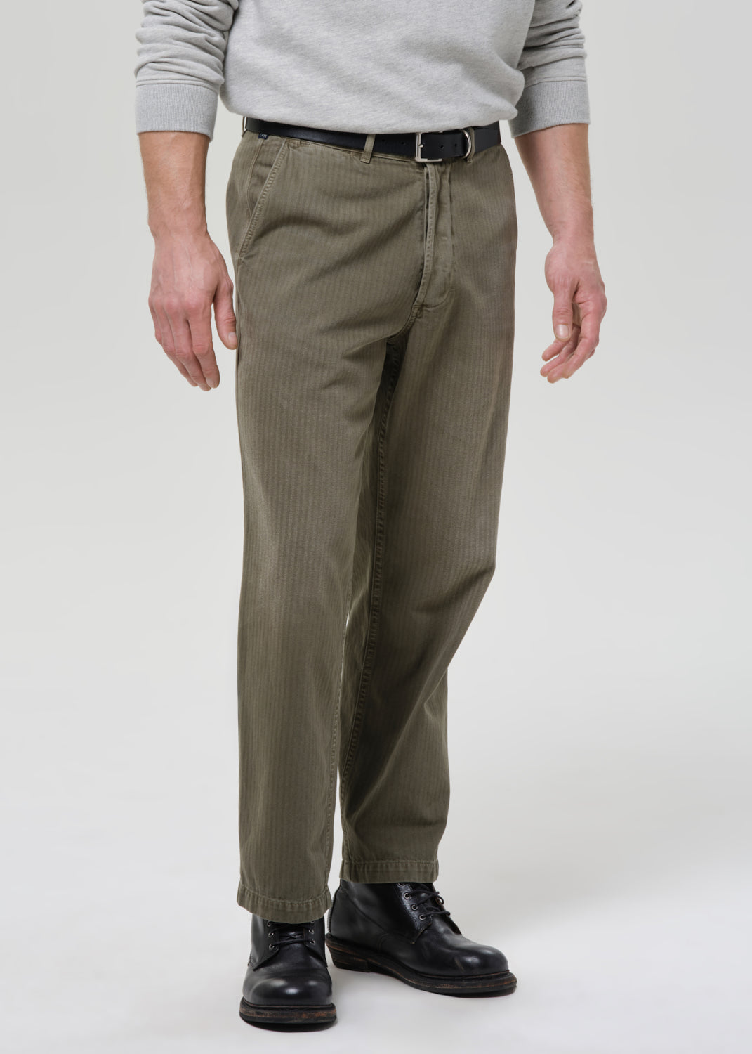 Person wearing khaki pants and black shoes on a grey background
