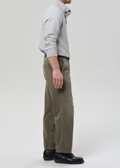Person wearing a gray sweater and green pants on a grey background
