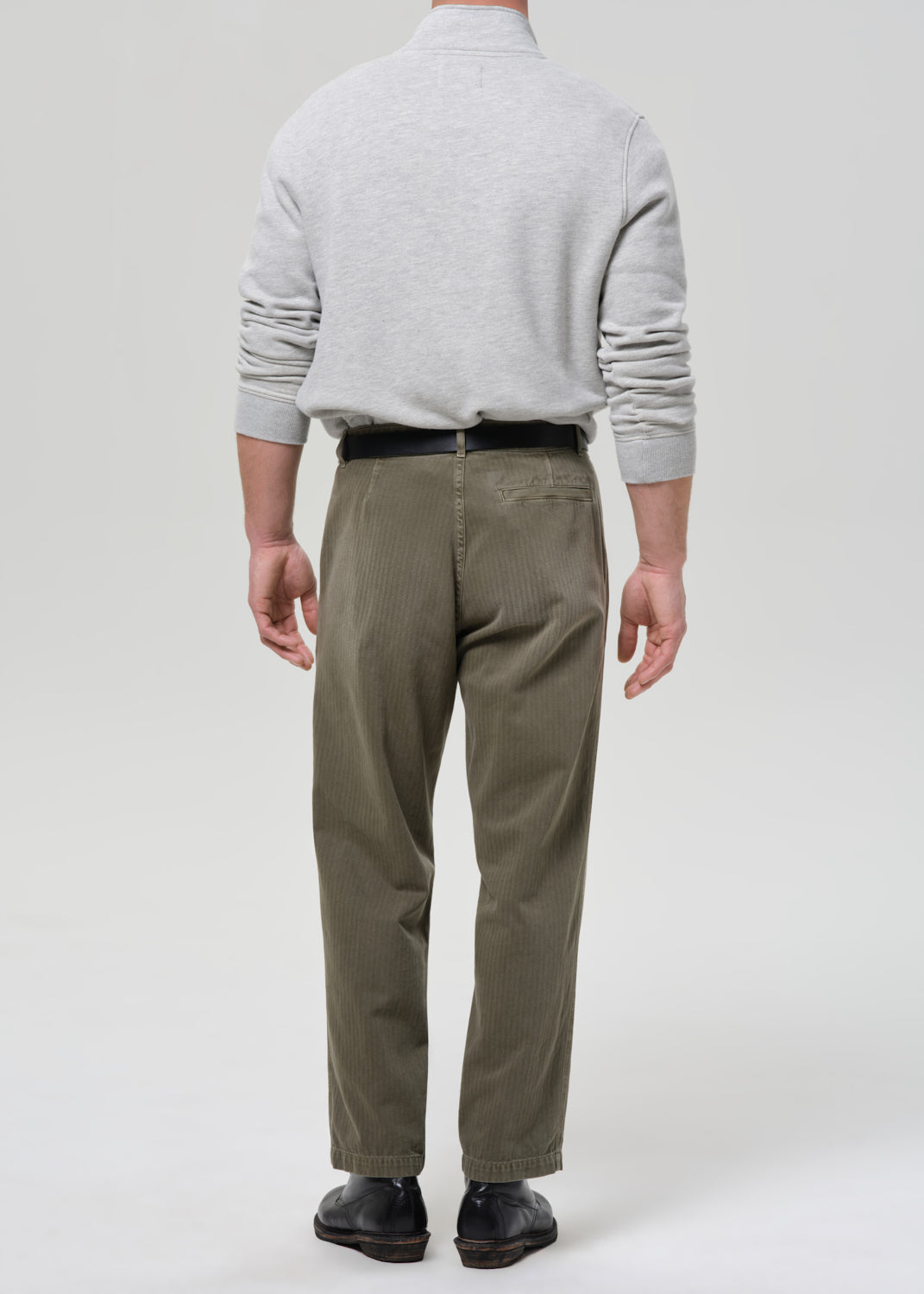 Person wearing a gray sweater and green pants on a grey background