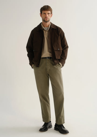Person wearing olive green relaxed straight leg pants with a dark brown jacket and black boots, front full body view on a light grey background.