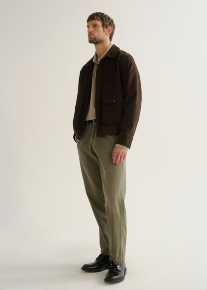 Person wearing olive green relaxed straight leg pants with a dark brown jacket and black boots, angled front full body view on a light grey background.