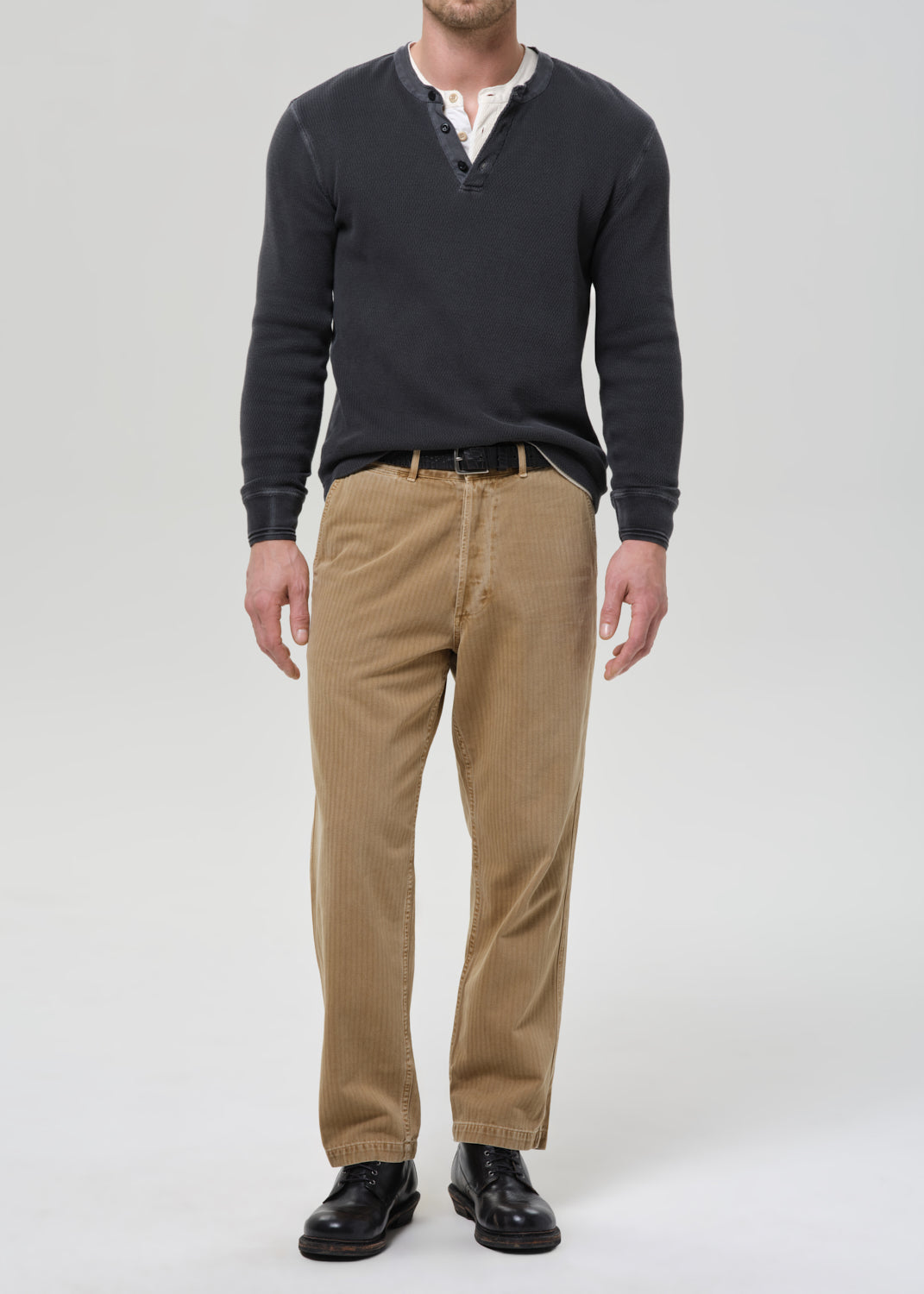 Man wearing a dark sweater, beige pants, and black shoes on a grey background