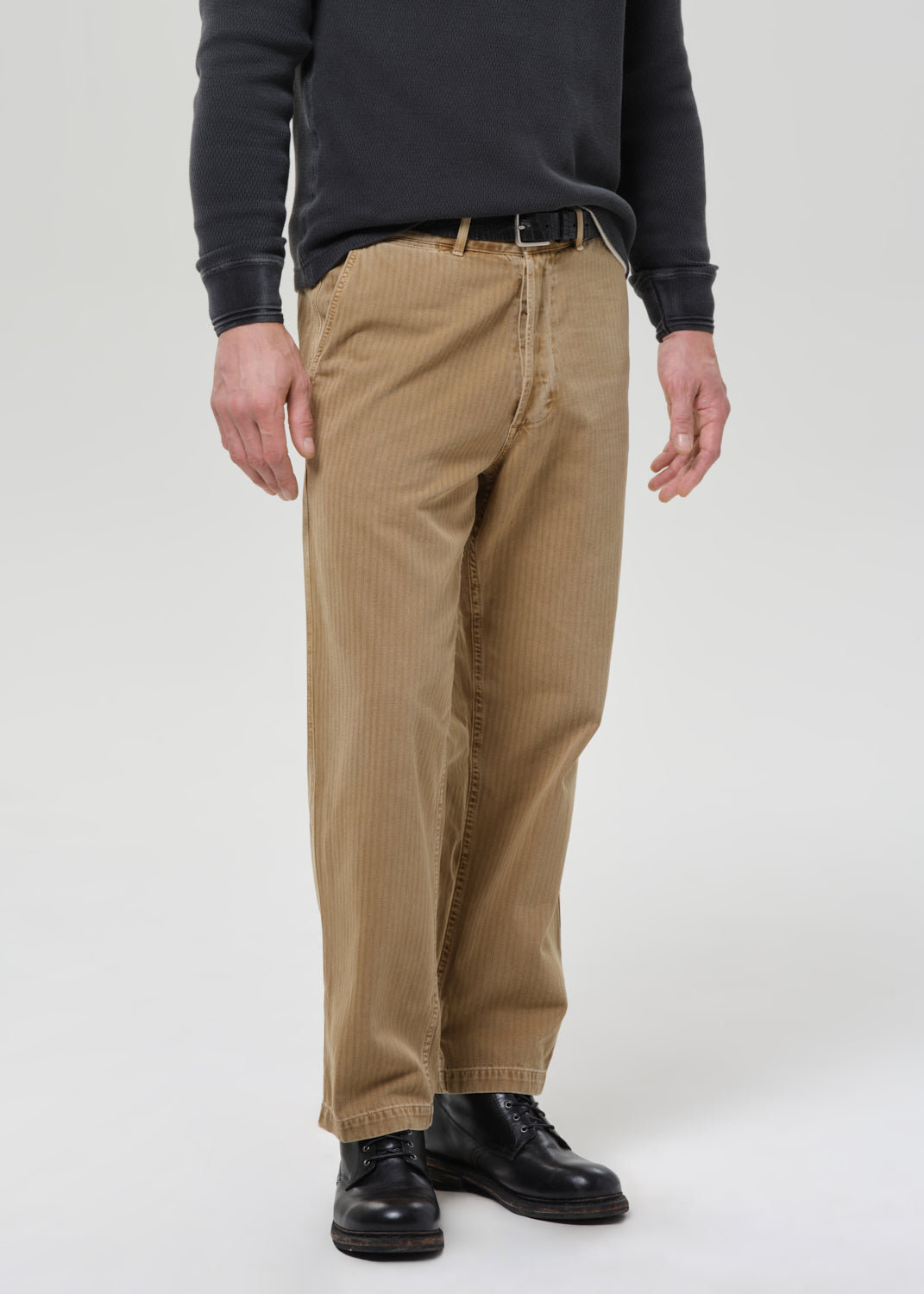 Person wearing beige corduroy pants and black shoes on a grey background