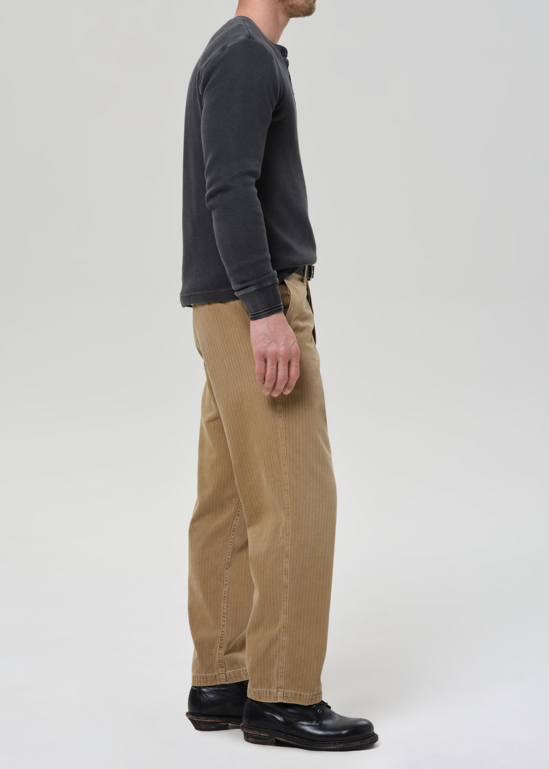 Person wearing a dark long-sleeve shirt and beige pants on a grey background