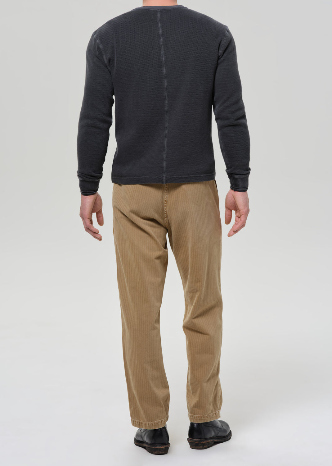 Person wearing a black long-sleeve shirt and beige pants on a grey background