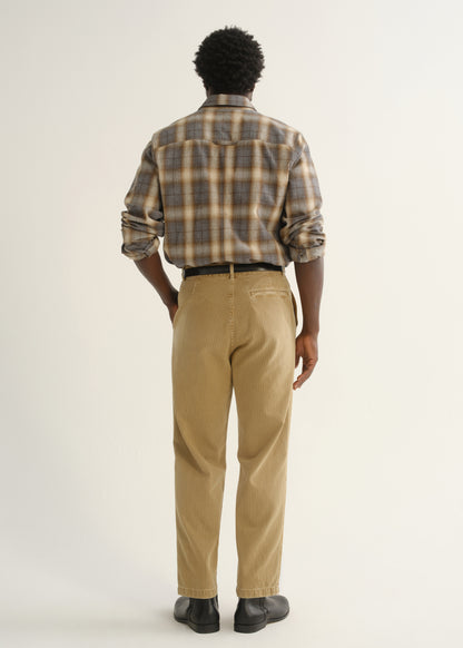 Person wearing tan straight leg corduroy pants with a multicolor plaid button-up shirt and black shoes, back full body view on a light grey background.