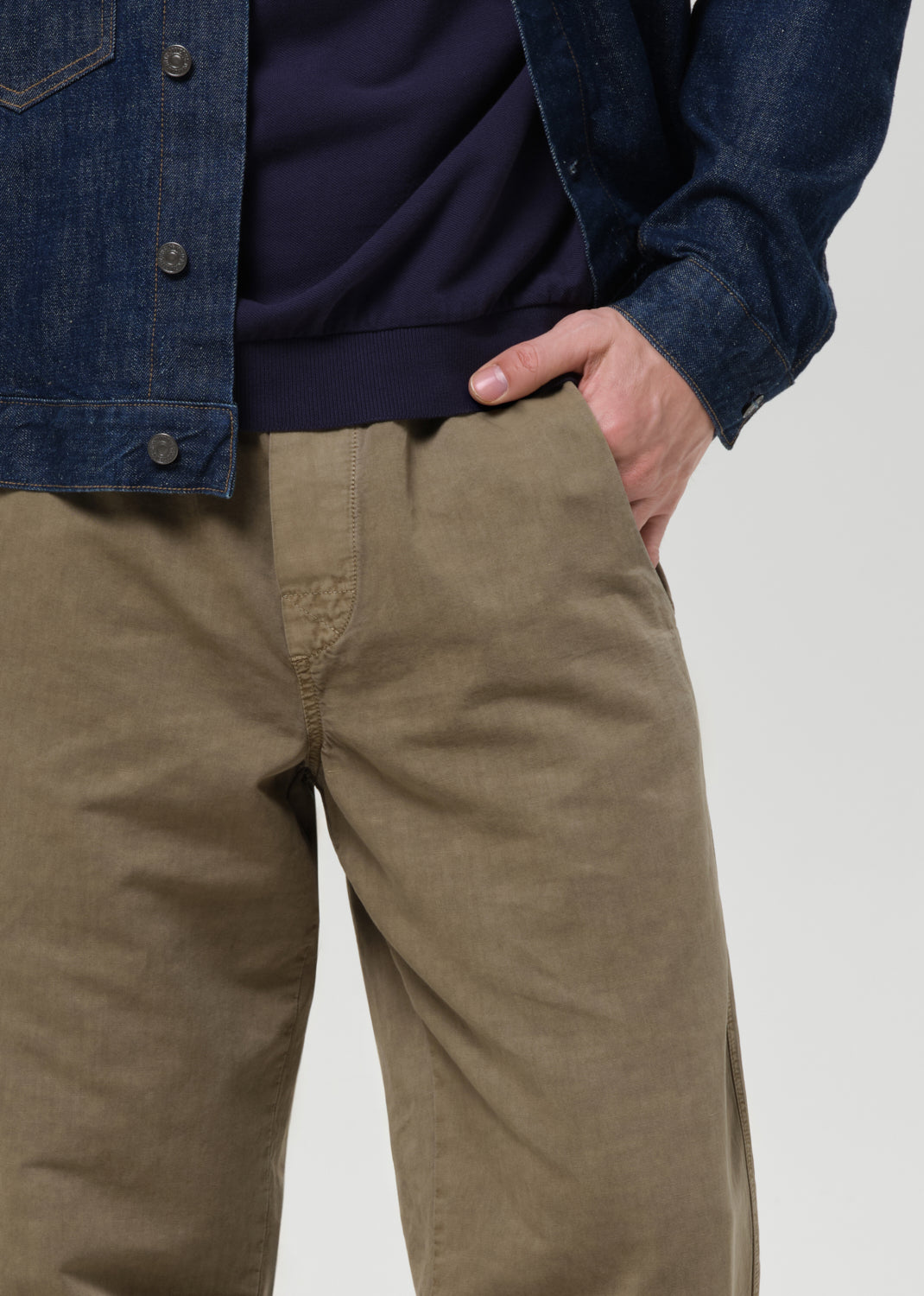 Person wearing a dark denim jacket, navy shirt, and beige pants on a plain background