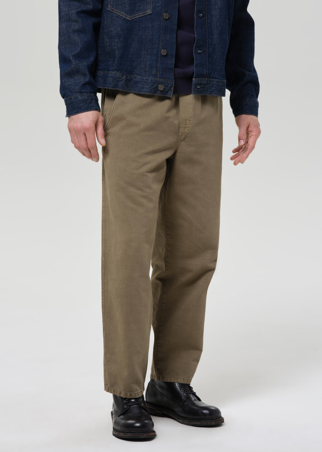 Person wearing a dark denim jacket, navy shirt, and beige pants on a plain background