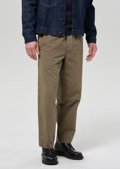 Person wearing a dark denim jacket, navy shirt, and beige pants on a plain background