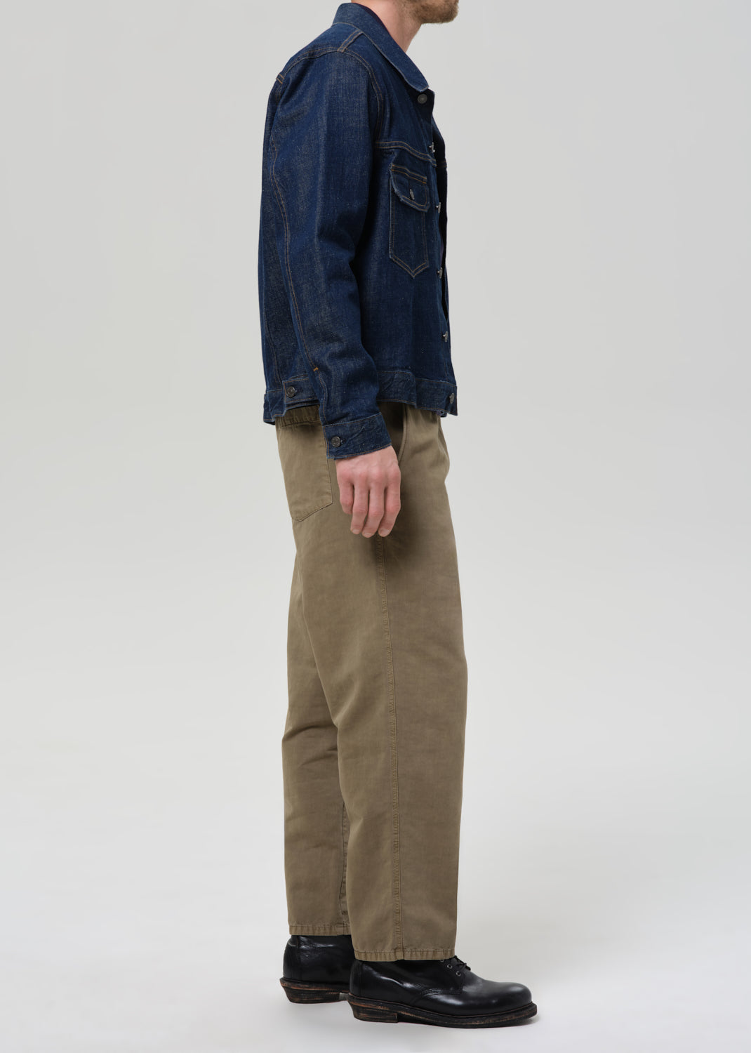Person wearing a dark denim jacket, navy shirt, and beige pants on a plain background