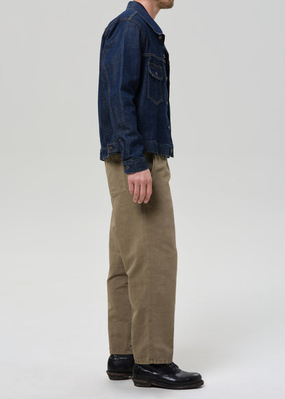 Person wearing a dark denim jacket, navy shirt, and beige pants on a plain background