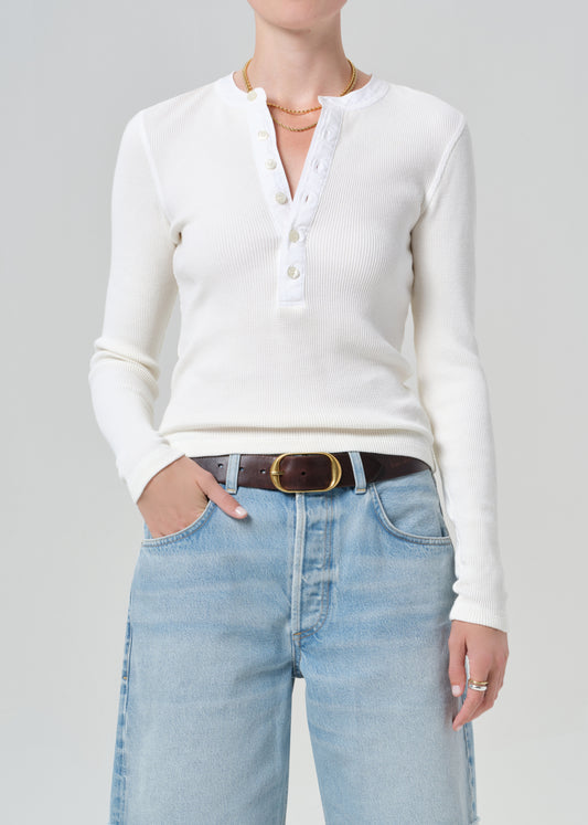 Person wearing a white long-sleeve shirt and light blue jean shorts on a gray background