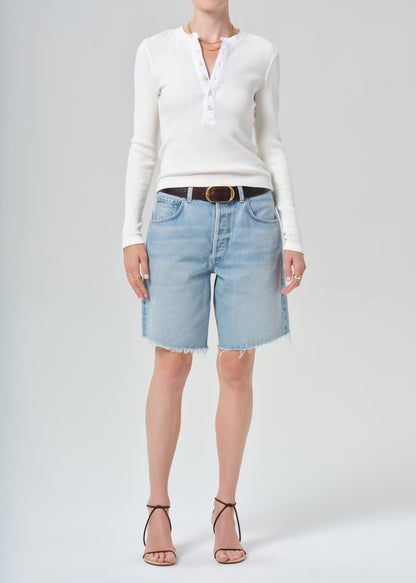 Person wearing a white long-sleeve shirt and light blue jean shorts on a gray background