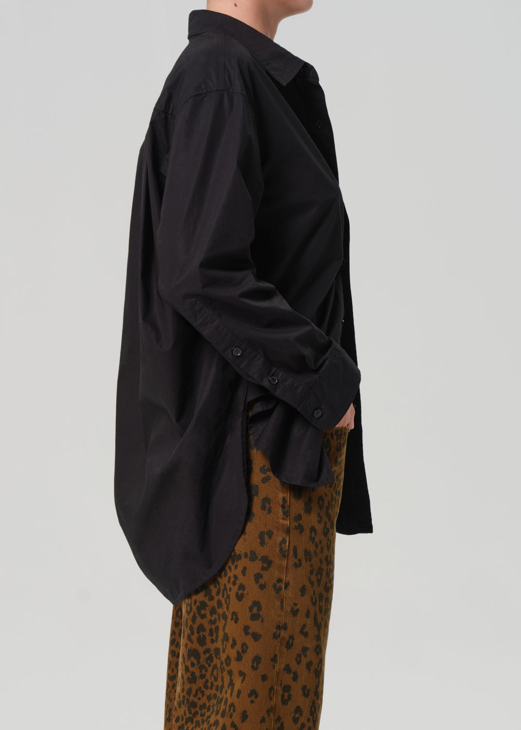 Person wearing a black oversized shirt with a cheetah print pant on a plain background