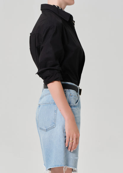 Person wearing a black shirt and light blue denim skirt on a plain background
