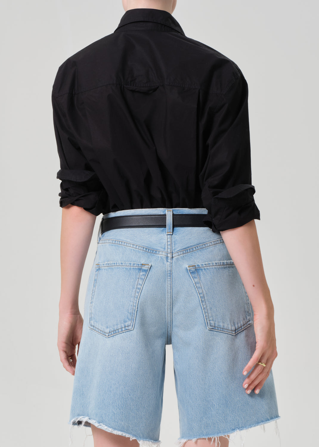 Person wearing a black shirt and light blue denim shorts on a plain background