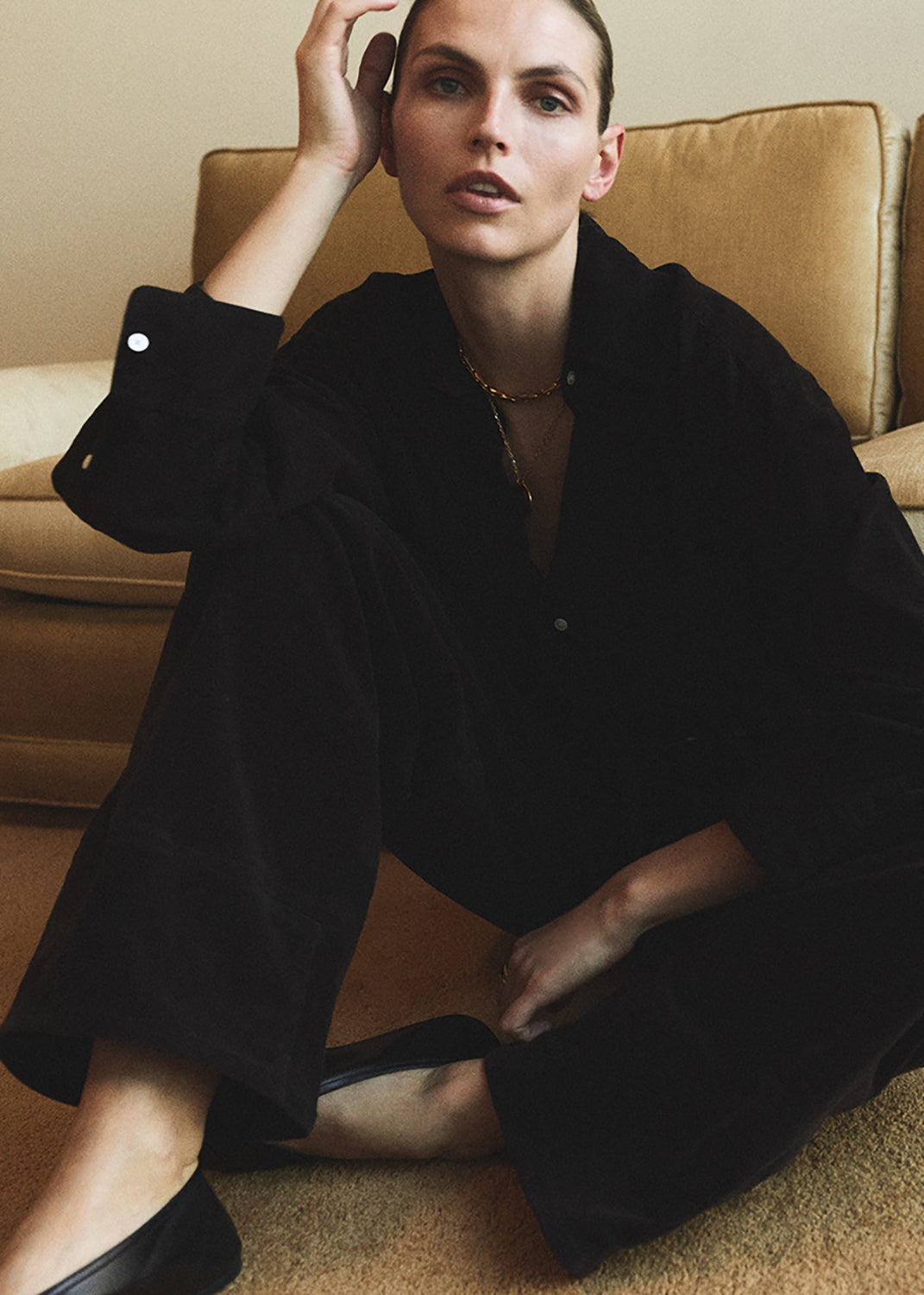 Person wearing a dark brown corduroy outfit sitting on a beige couch.