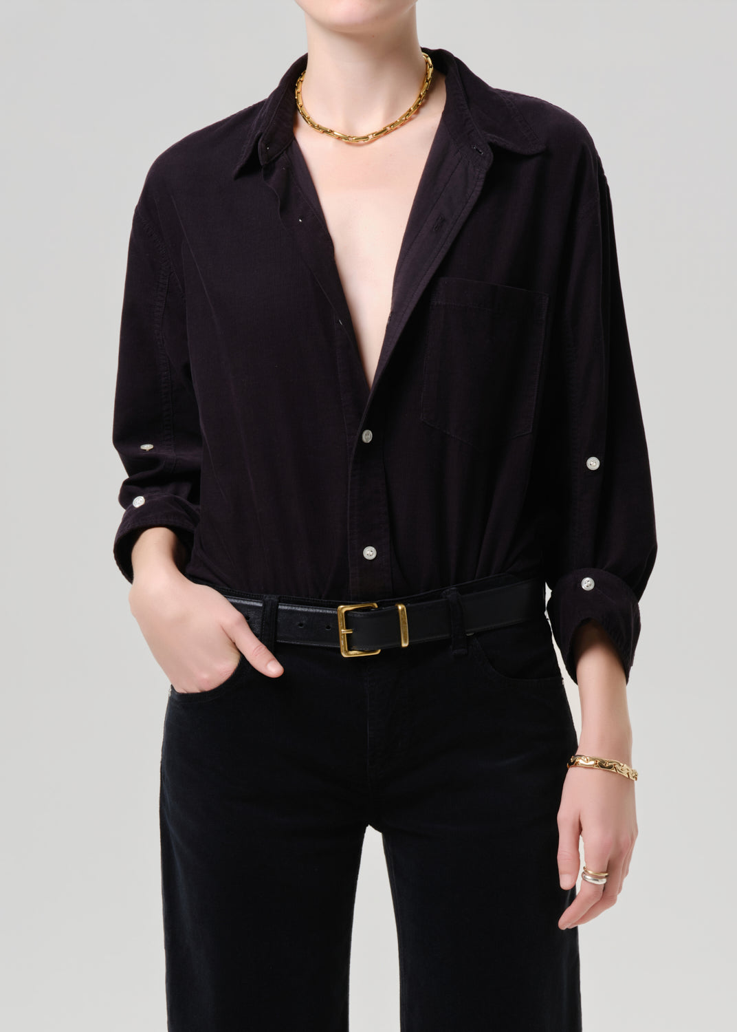 Person wearing a dark grey button-up shirt with a plunging neckline and gold jewelry on a grey background