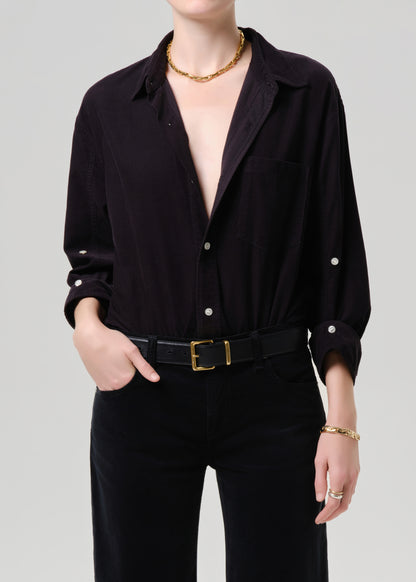 Person wearing a dark grey button-up shirt with a plunging neckline and gold jewelry on a grey background