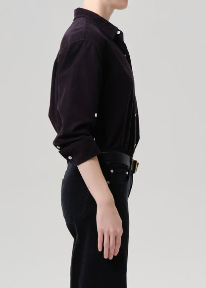 Person wearing a dark grey shirt with rolled-up sleeves on a grey background
