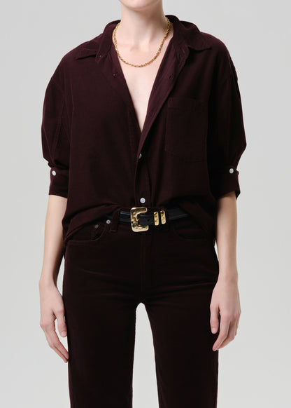 Person wearing a dark purple shirt with short sleeves and a gold belt on a grey background