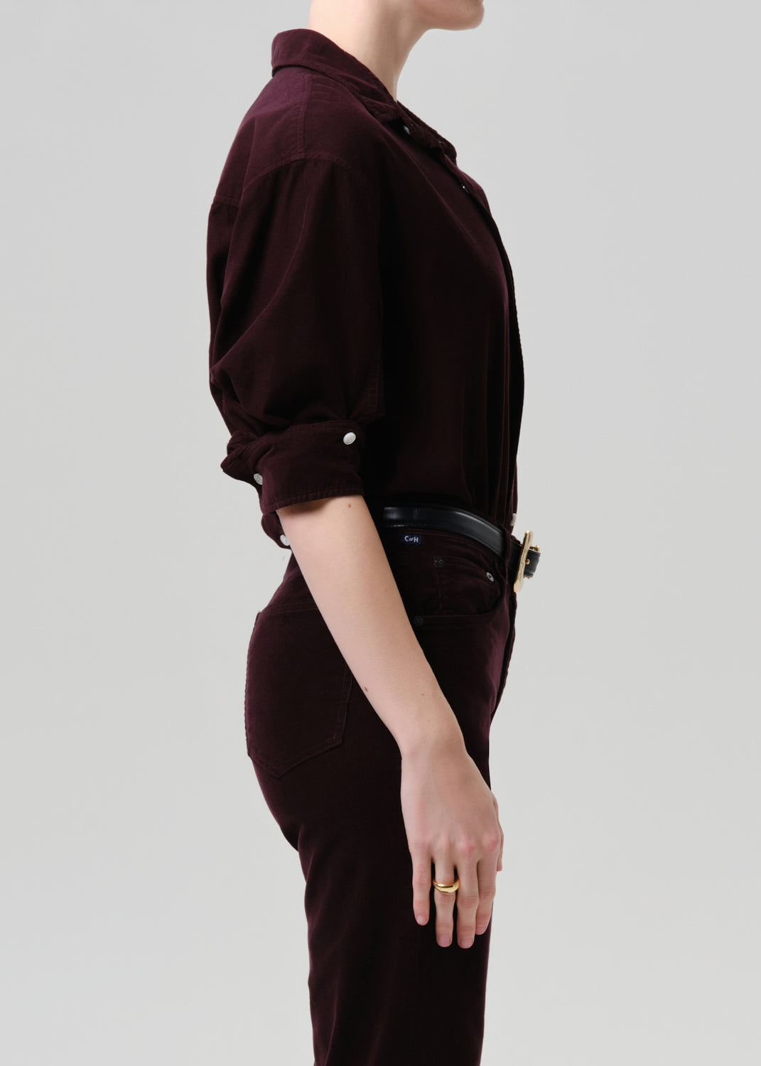 Person wearing a dark purple  outfit with a belt on a light grey background