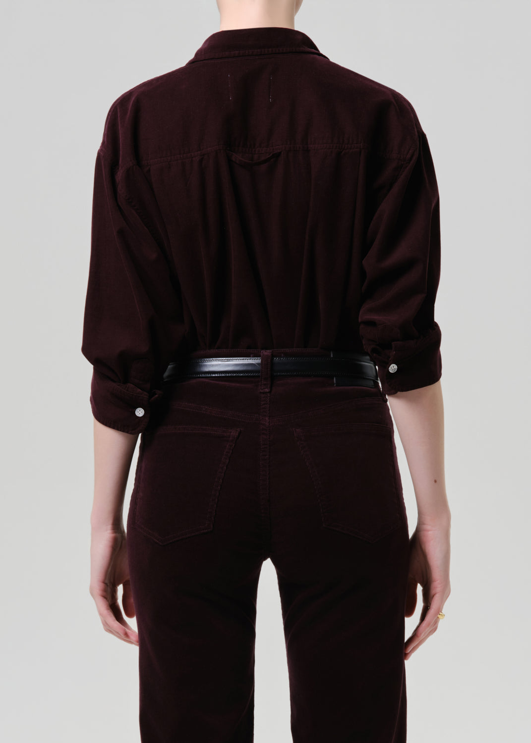 Person wearing a dark purple shirt and pants on a grey background