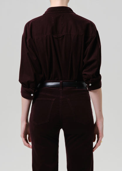 Person wearing a dark purple shirt and pants on a grey background