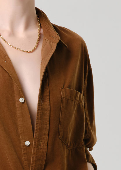 Brown shirt worn by a mannequin with a gold necklace on a grey background