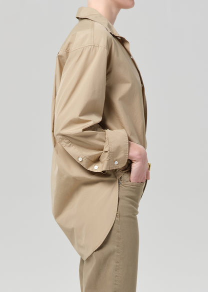 Person wearing a beige jacket and pants on a light gray background
