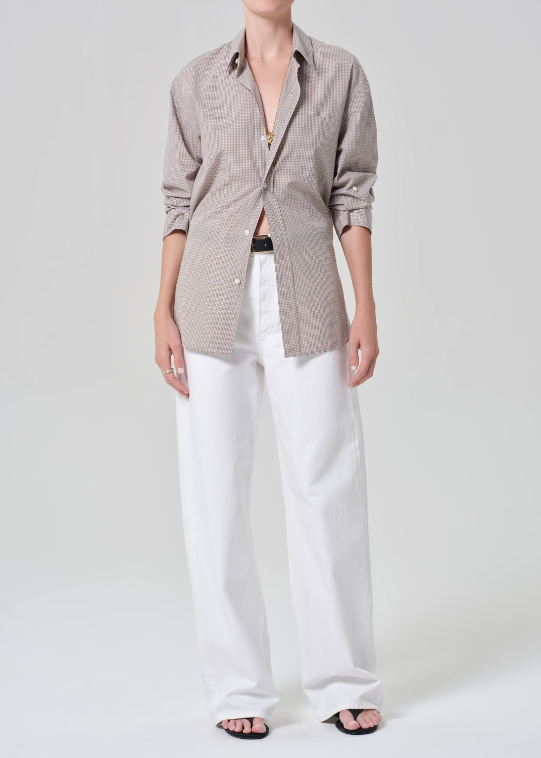 Person wearing a light brown plaid shirt with rolled-up sleeves and white pants on a plain background