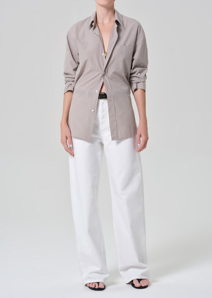 Person wearing a light brown plaid shirt with rolled-up sleeves and white pants on a plain background