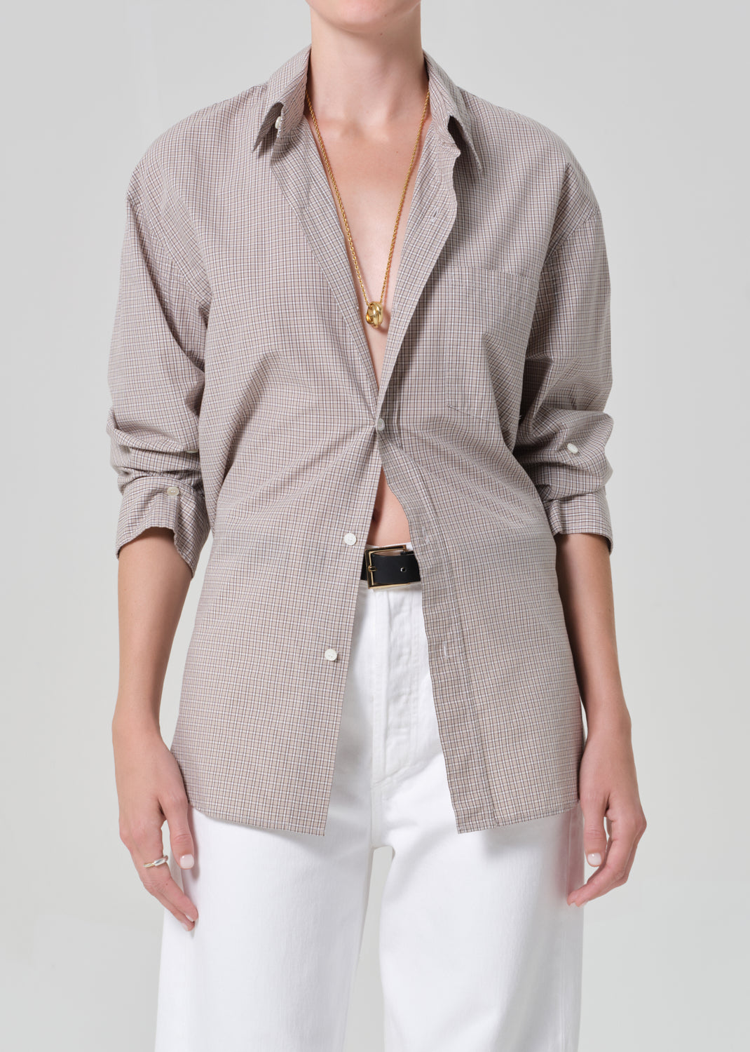 Person wearing a light brown plaid shirt with rolled-up sleeves and white pants on a plain background