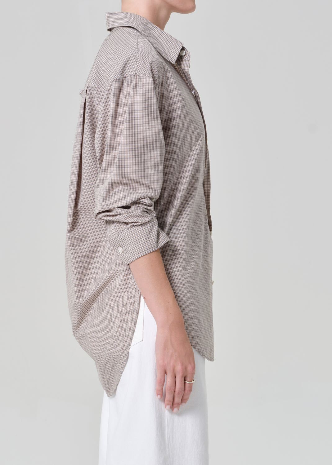 Person wearing a light brown plaid shirt with rolled-up sleeves and white pants on a plain background