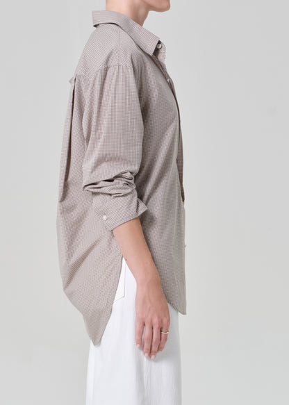 Person wearing a light brown plaid shirt with rolled-up sleeves and white pants on a plain background