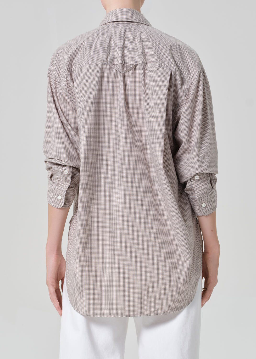 Person wearing a light brown plaid shirt with rolled-up sleeves and white pants on a plain background