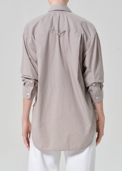 Person wearing a light brown plaid shirt with rolled-up sleeves and white pants on a plain background