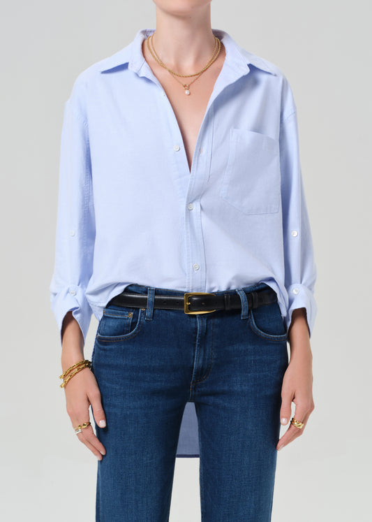 Person wearing a light blue button-up shirt and blue jeans on a plain background