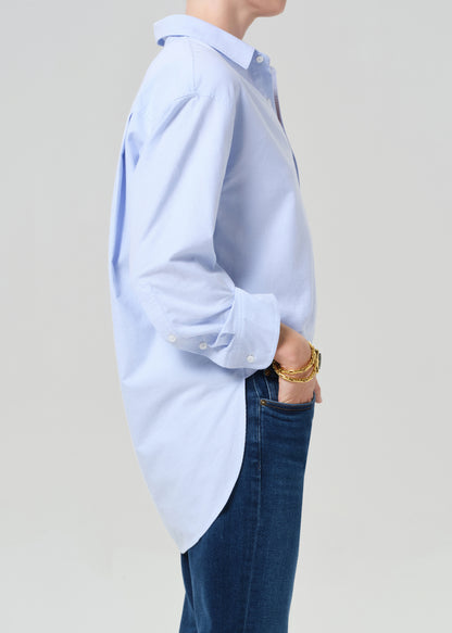 Person wearing a light blue button-up shirt and dark jeans on a plain background