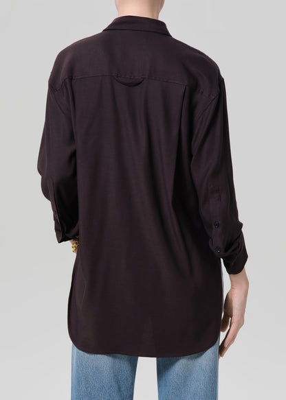 Person wearing a brown shirt and blue jeans with gold jewelry on a plain background