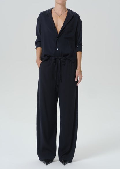A model wearing a dark navy blue wide-leg jumpsuit with a button-down shirt collar and drawstring waist, photographed against a  background.