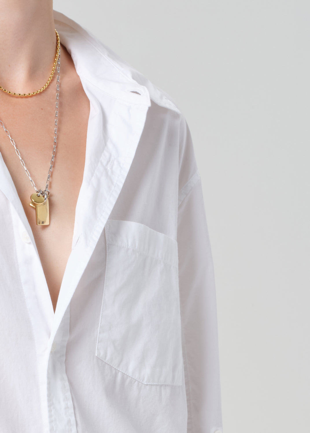 Person wearing a white shirt with gold necklaces on a plain background
