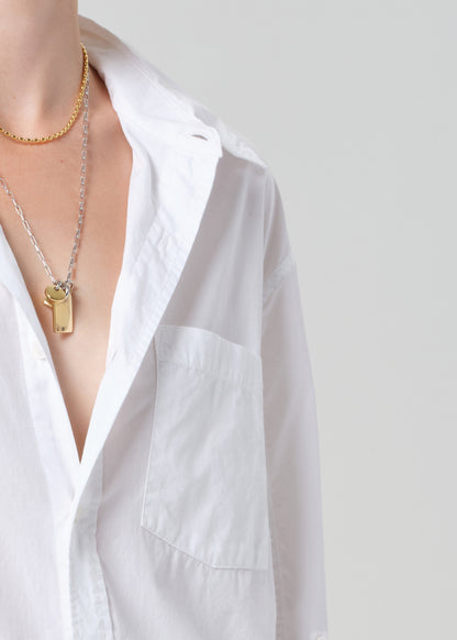 Person wearing a white shirt with gold necklaces on a plain background