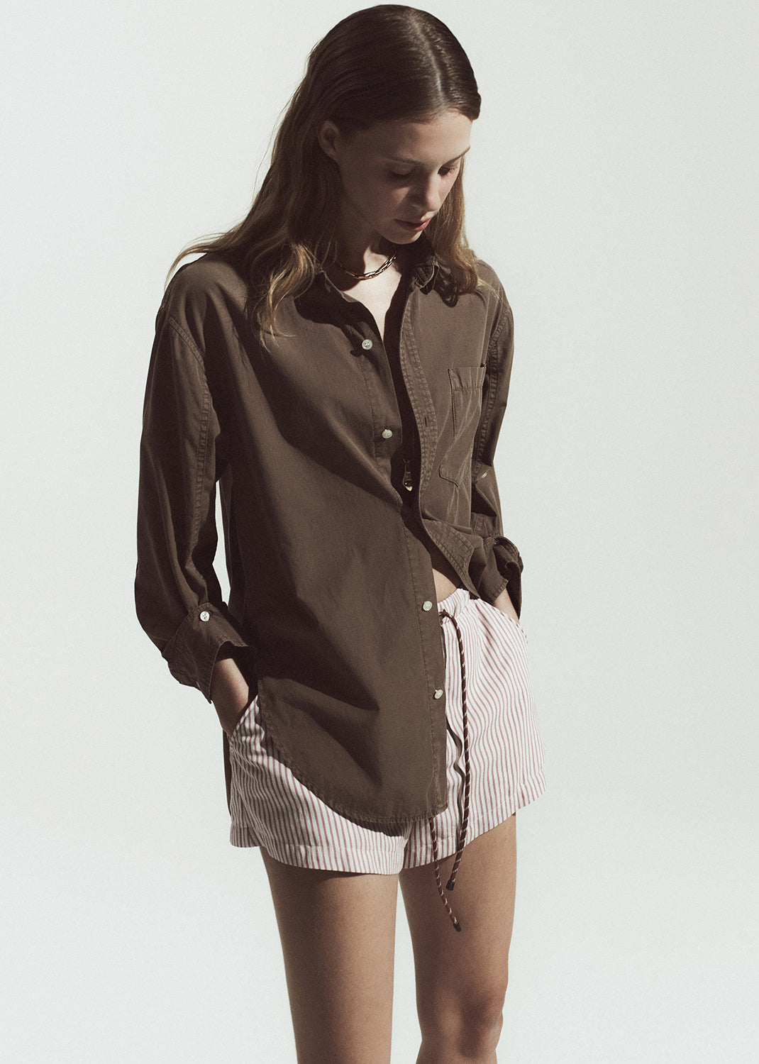 Woman wearing a brown shirt over a white top with a striped shorts on a plain background
