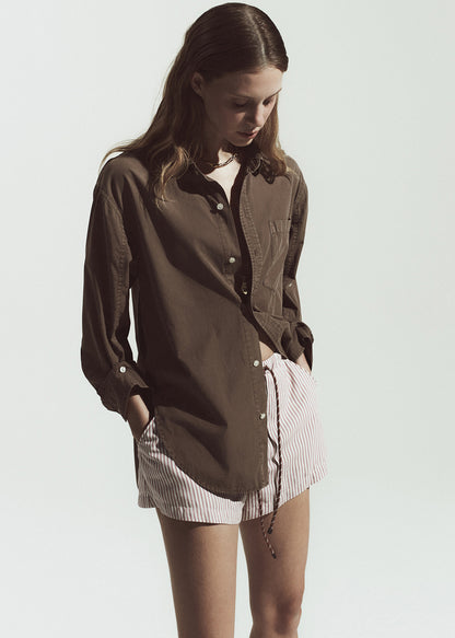 Woman wearing a brown shirt over a white top with a striped shorts on a plain background