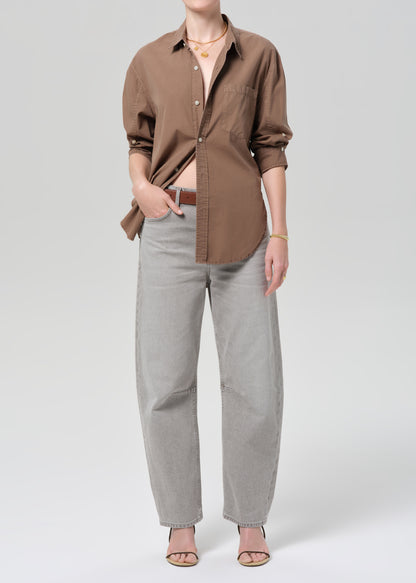Person wearing a brown shirt with light gray jeans on a plain background