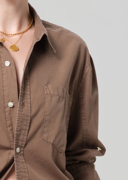 Person wearing a brown shirt with light gray jeans on a plain background