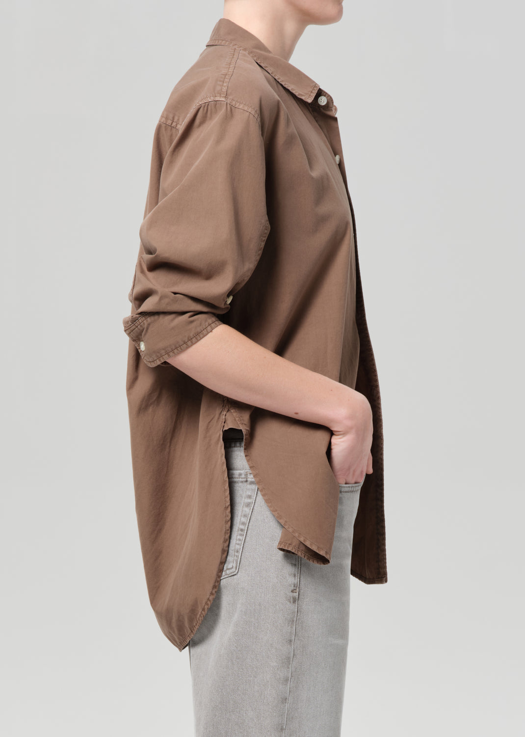 Person wearing a brown shirt with light gray jeans on a plain background