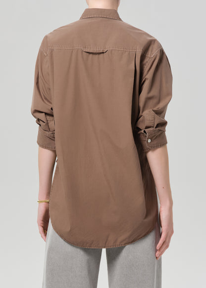 Person wearing a brown shirt with light gray jeans on a plain background