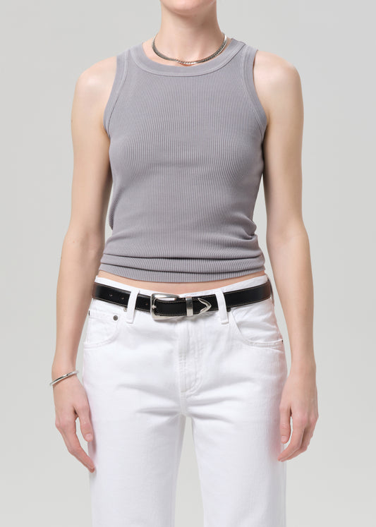 Person wearing a gray sleeveless top and white pants on a plain background